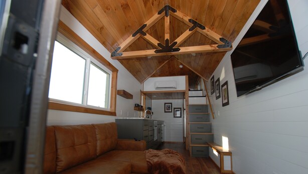 Un espacio habitable compacto con techo de madera, un sofá, una zona de cocina y una escalera que lleva a un nivel superior.