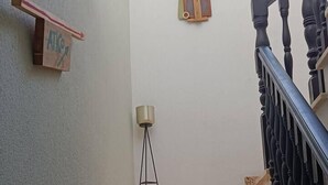 A staircase with wooden steps and black balusters, a small shelf with a sign, and a floor lamp against a plain wall. - Penthouse in Ciudad Vieja (Cordoba)