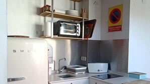 A compact kitchen with a white refrigerator, a built-in oven, a microwave, a sink, and a small countertop. There are shelves above the sink holding various kitchen items. - Penthouse in Ciudad Vieja (Cordoba)
