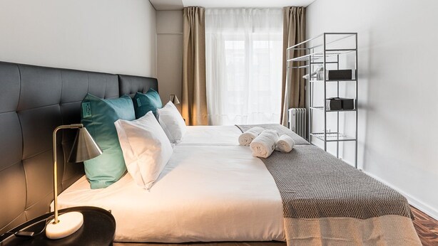 A modern hotel room with a large bed, a bedside lamp, a wardrobe, and a view of the city through the window.