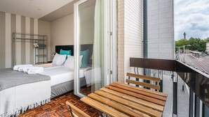 A modern hotel room with a bed, a seating area, and a view of the cityscape.
