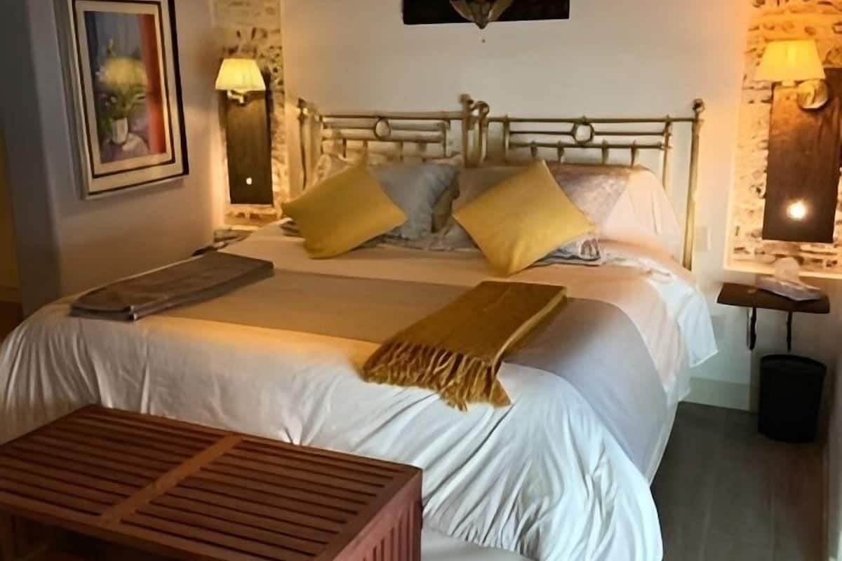 A bedroom with a wooden headboard, a bed with white linens and two yellow pillows, a wooden bench, and a patterned rug.