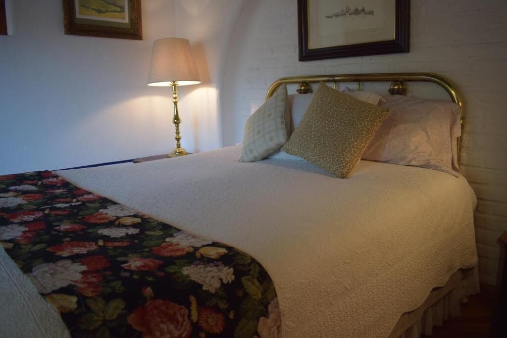 A neatly made bed with a floral bedspread, a lamp on the nightstand, and a framed picture on the wall.