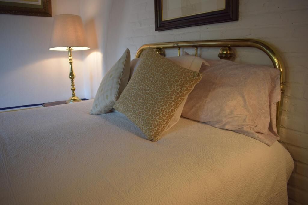 Una cama bien hecha con almohadones estampados, un cabecero de latón y una lámpara de noche.