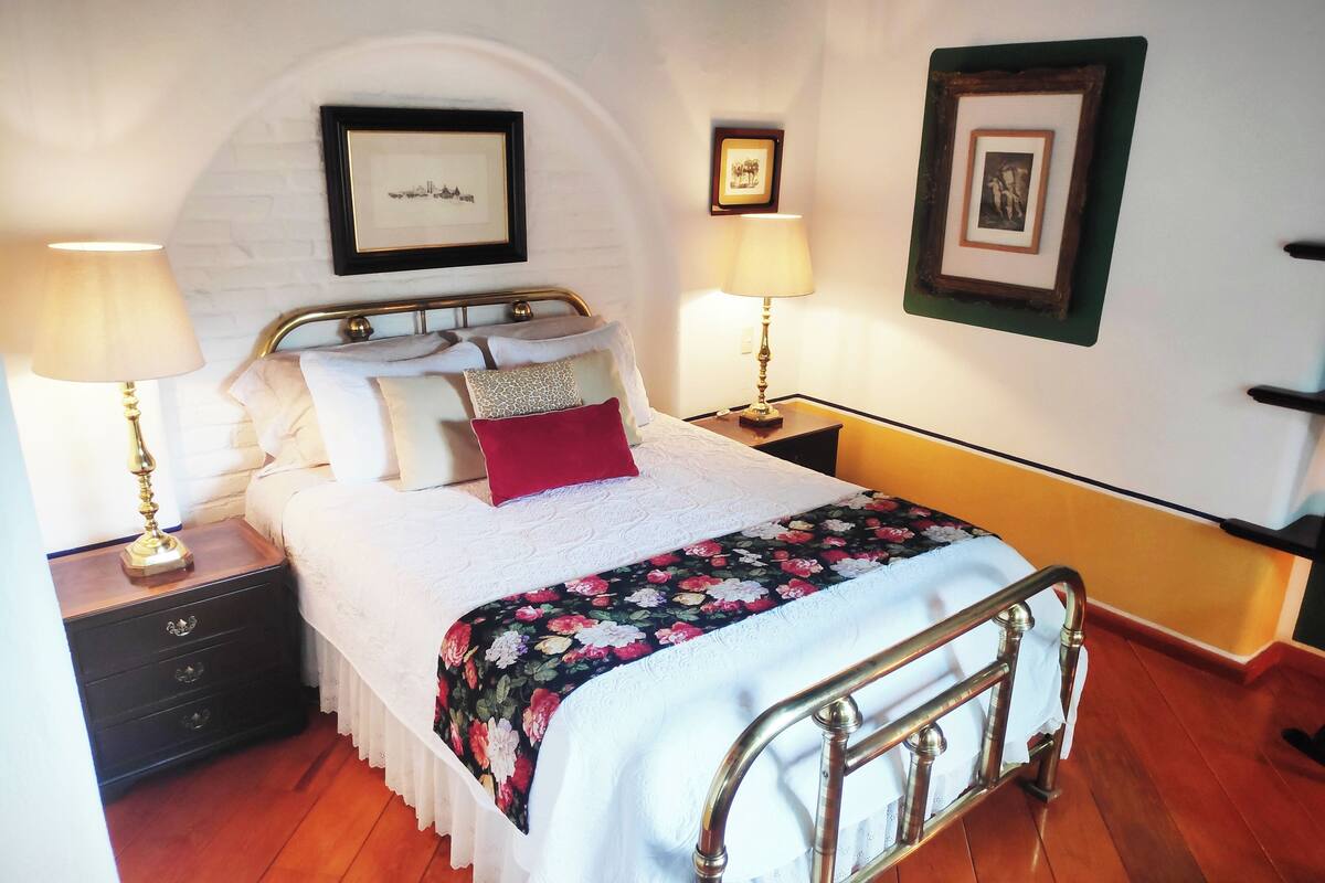 A neatly arranged bedroom with a bed, two bedside tables, a nightstand, and a wall-mounted shelf.