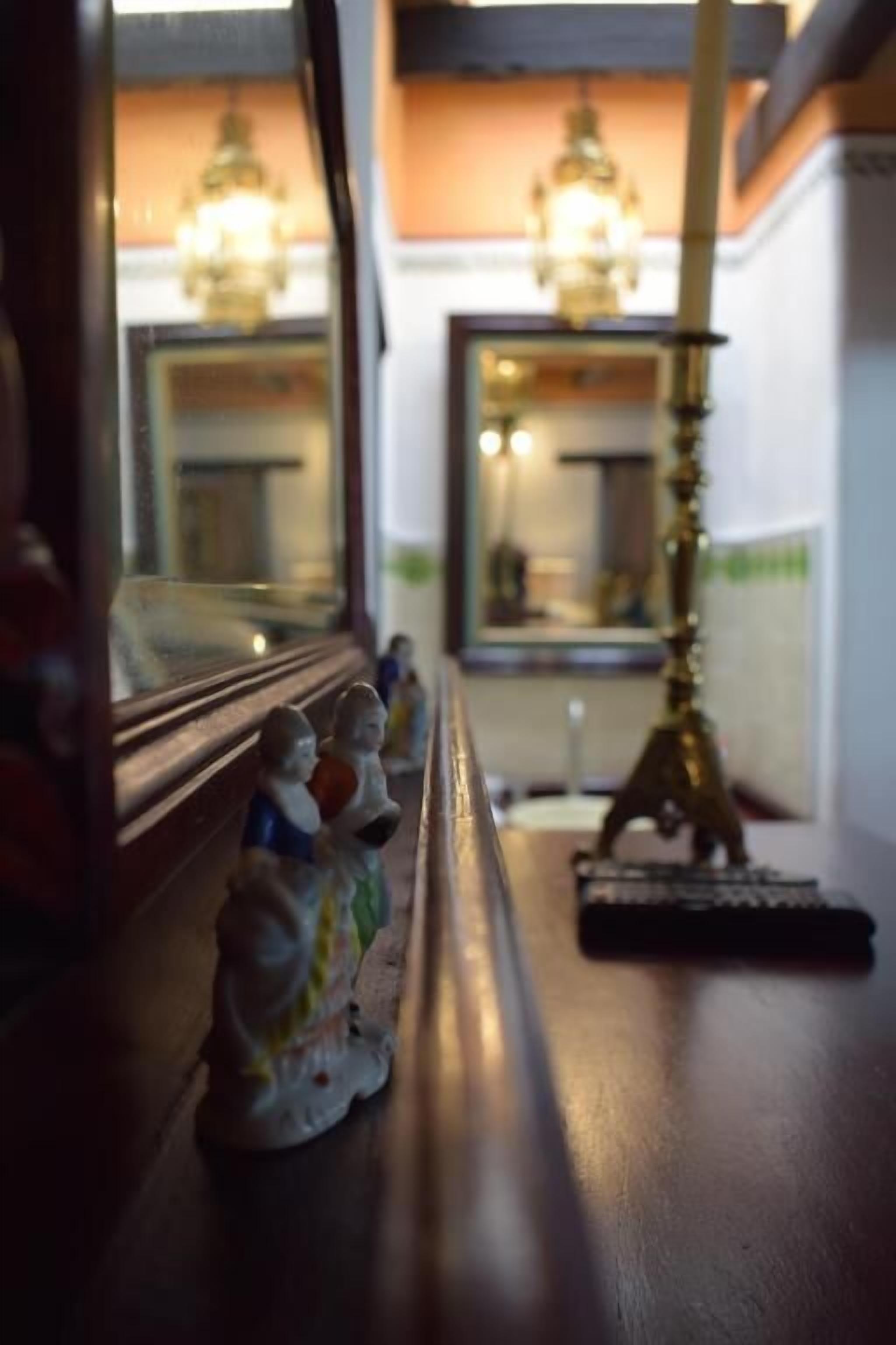 A view through a window with a wooden frame, featuring a small figurine on the sill and a brass lamp on the table.