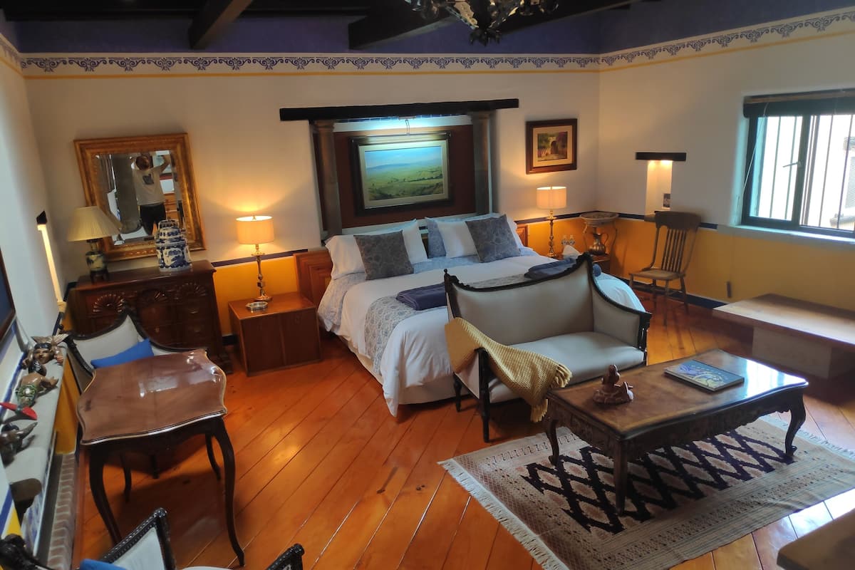 A bedroom with a bed, bedside tables, a chair, a sofa, a lamp, a picture frame, and a window.