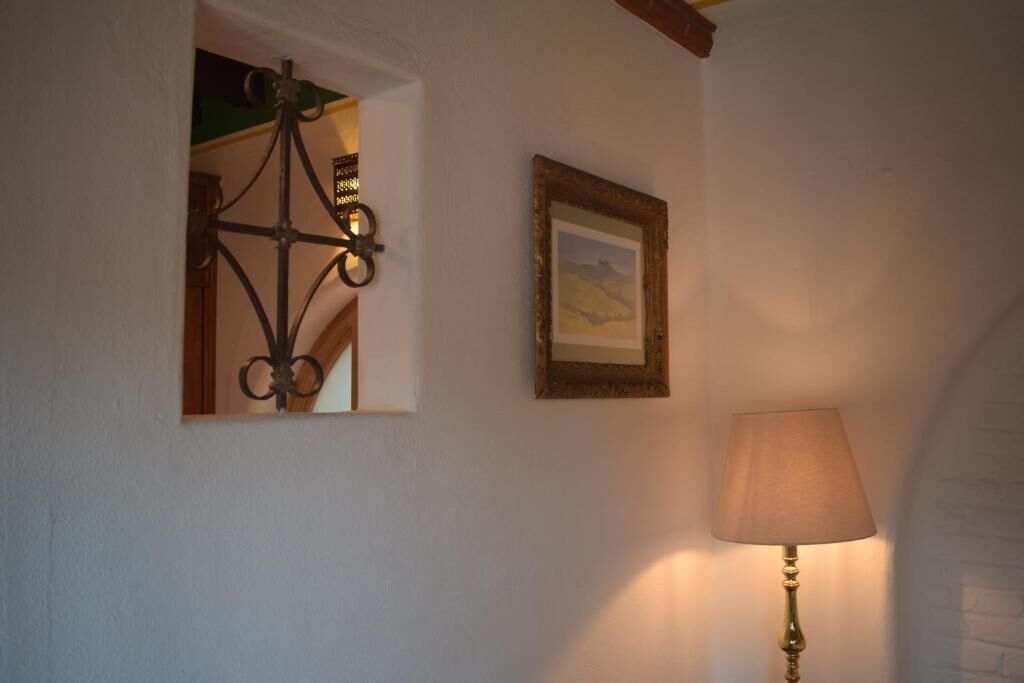 A room with a wall-mounted lamp, a framed picture, and a window with a decorative light fixture.
