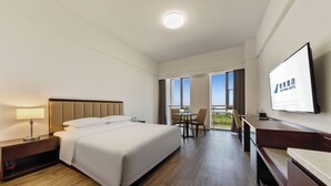 A hotel room with a bed, bedside table, lamp, TV, and a balcony with a view. - Beijing CSN Pearl Hotel (Langfang)