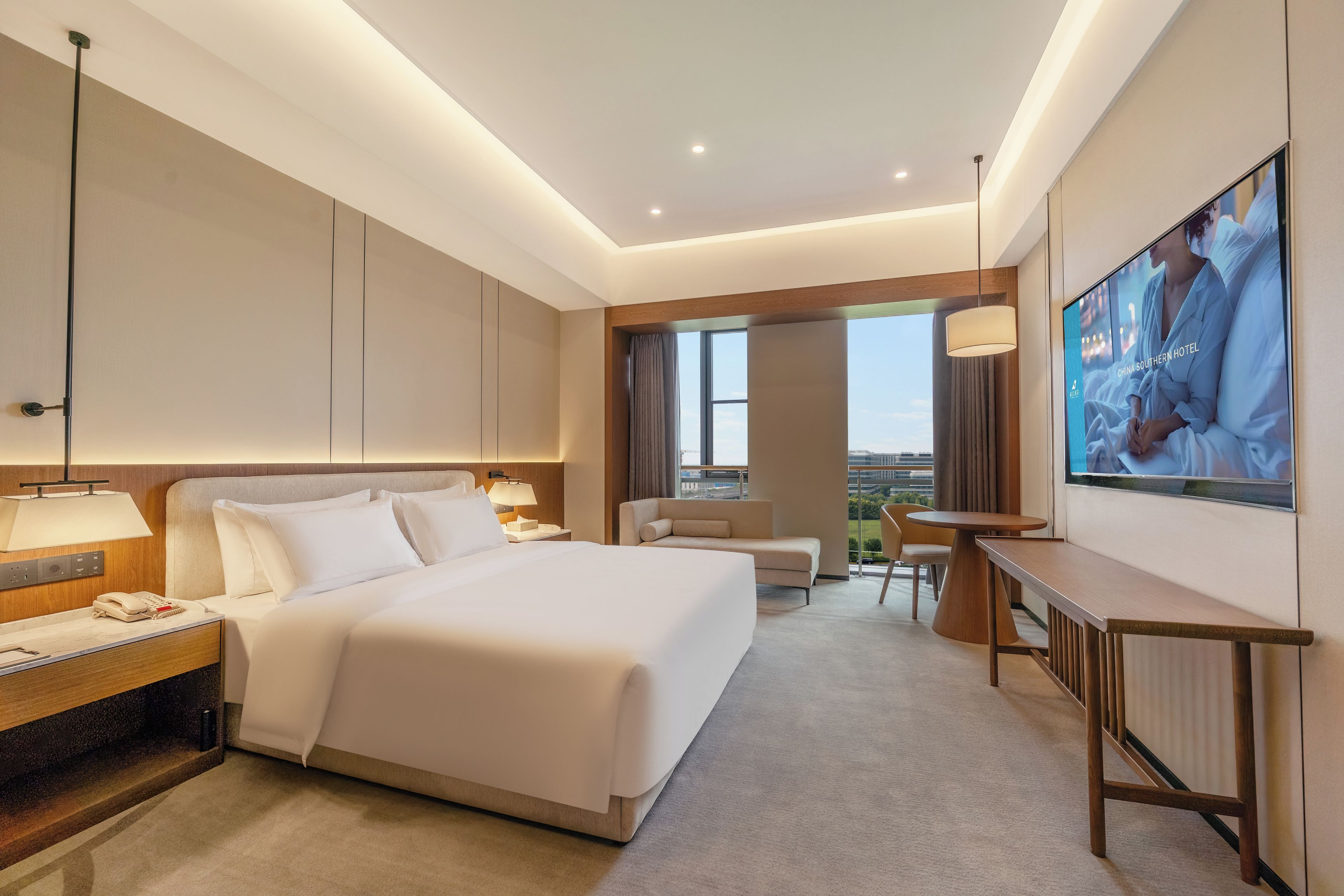 A modern hotel room with a large bed, bedside table, lamp, and a television on the wall.