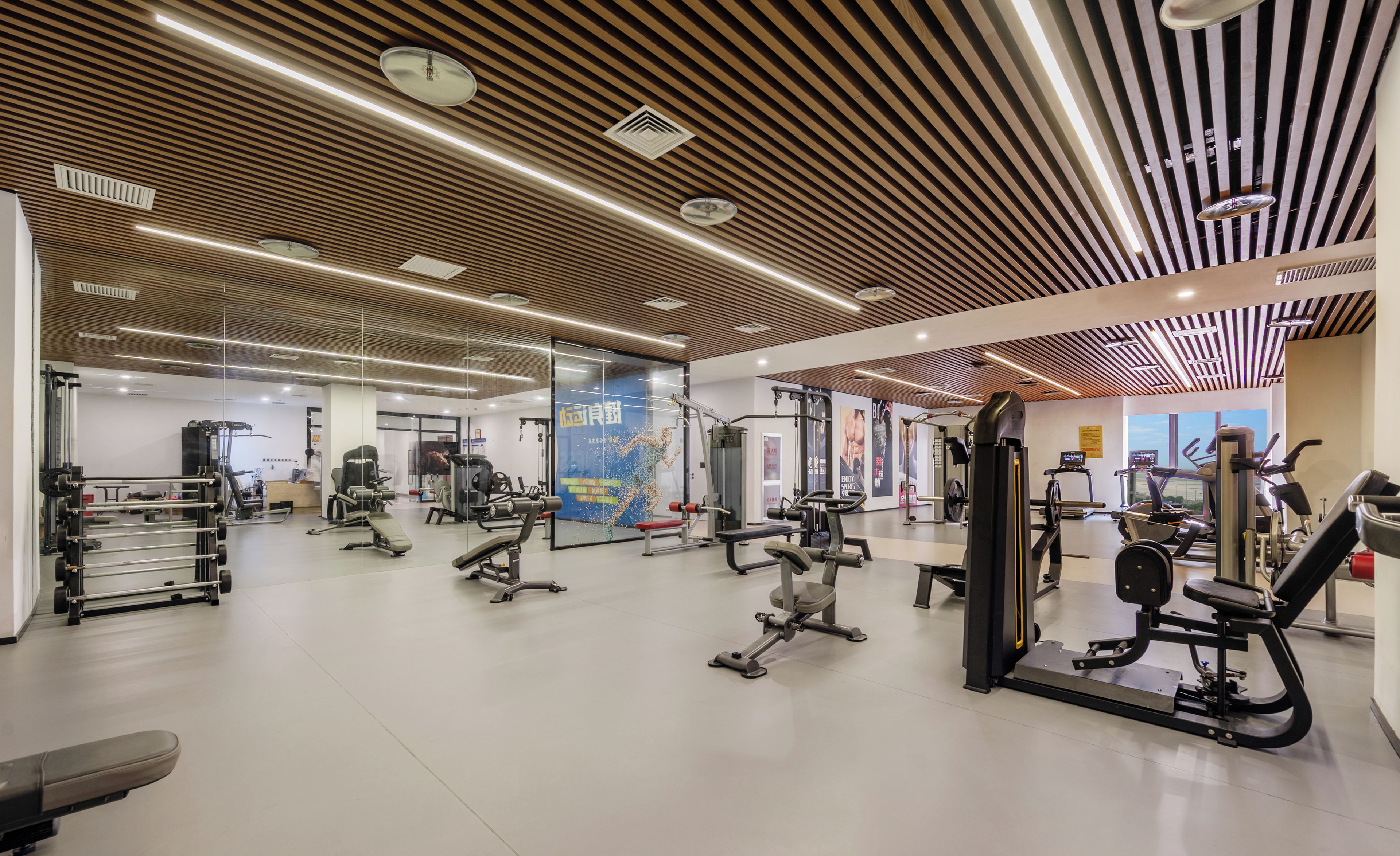 A modern gym with various exercise equipment, a wooden ceiling design, and a large mirror wall.