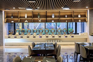 Un interior de restaurante moderno con una larga exhibición de platos decorativos, estanterías de madera con jarrones y un piso de mármol pulido.