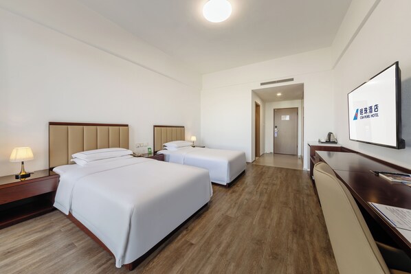 A hotel room with two beds, a desk, a chair, a TV, and a door leading to another room.