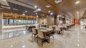 A spacious dining area with multiple tables and chairs, a long counter with food display, and a modern ceiling design. - Beijing CSN Pearl Hotel (Langfang)