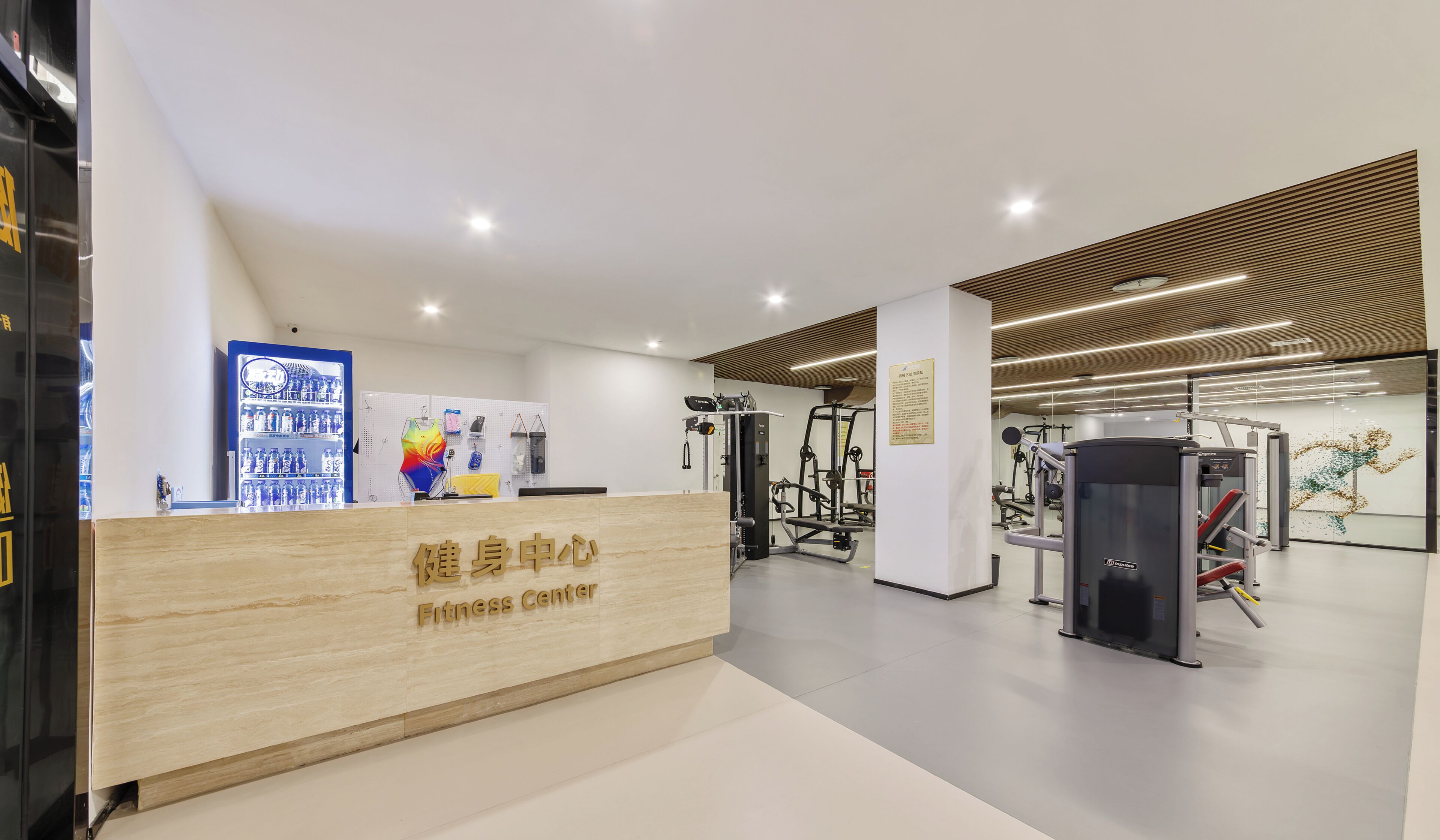 Un gimnasio con mostrador de recepción, máquinas de ejercicio y un mural temático de acondicionamiento físico.