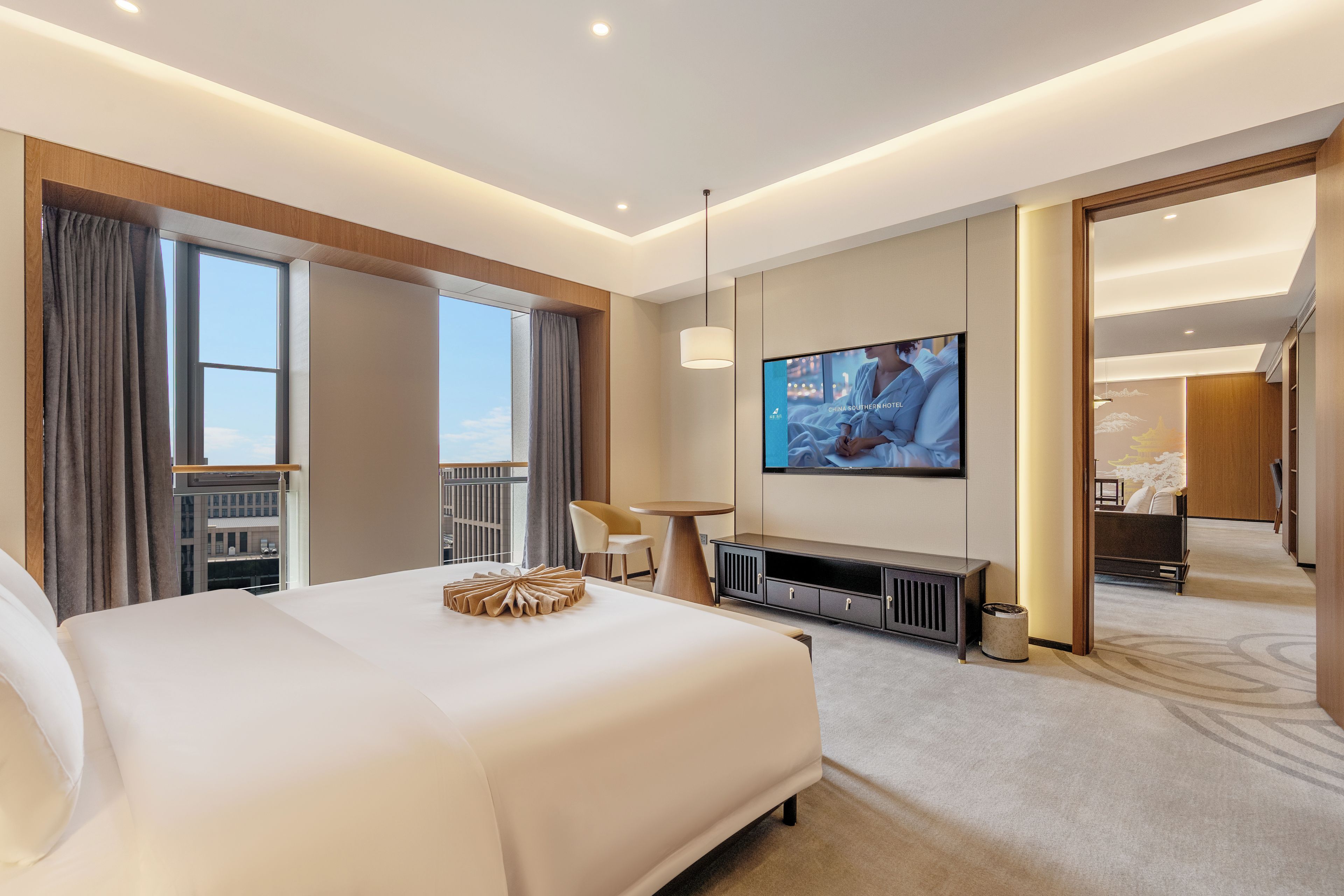 A hotel room with a large bed, a television, a desk, and a view of the city.