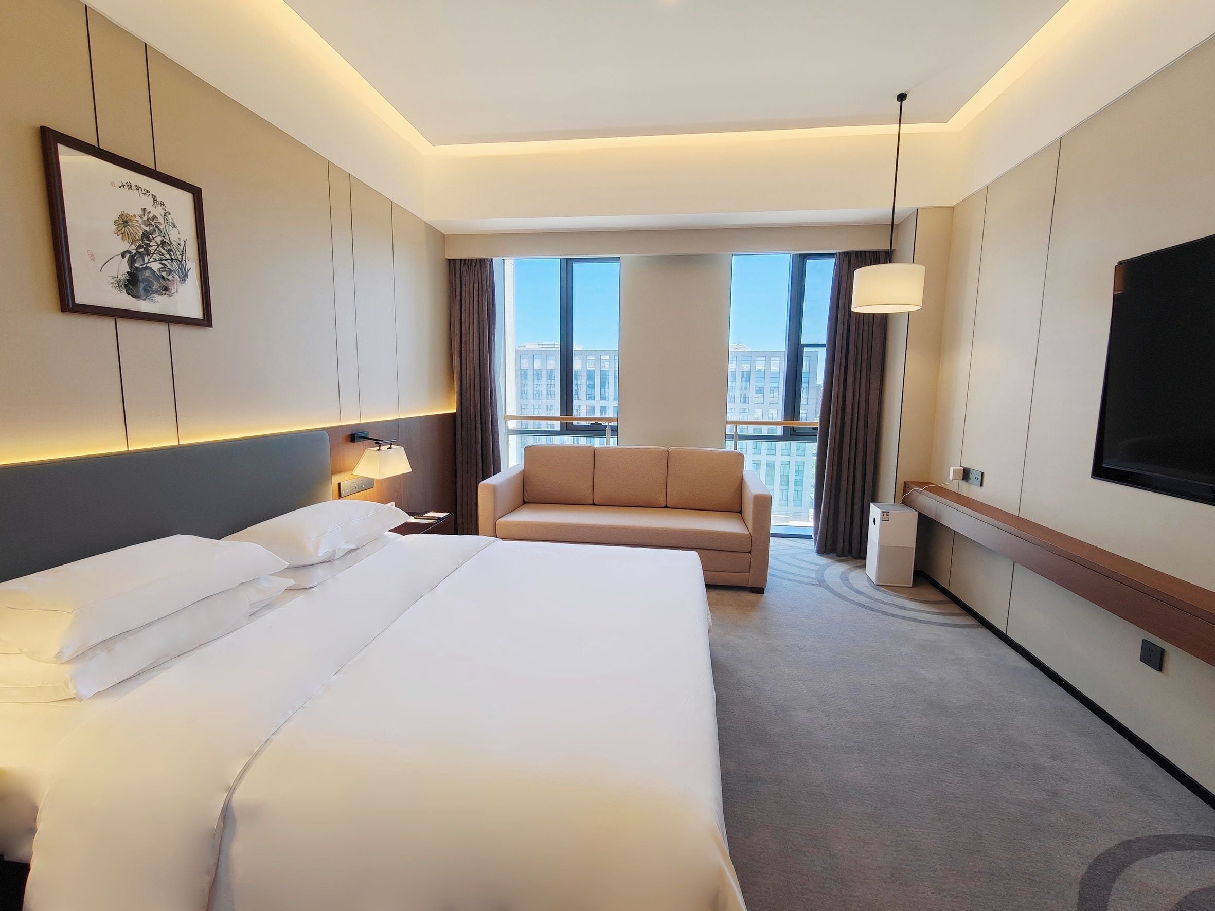 Una habitación de hotel con una cama grande, un sofá, un escritorio, un televisor y una ventana con vista a la ciudad.
