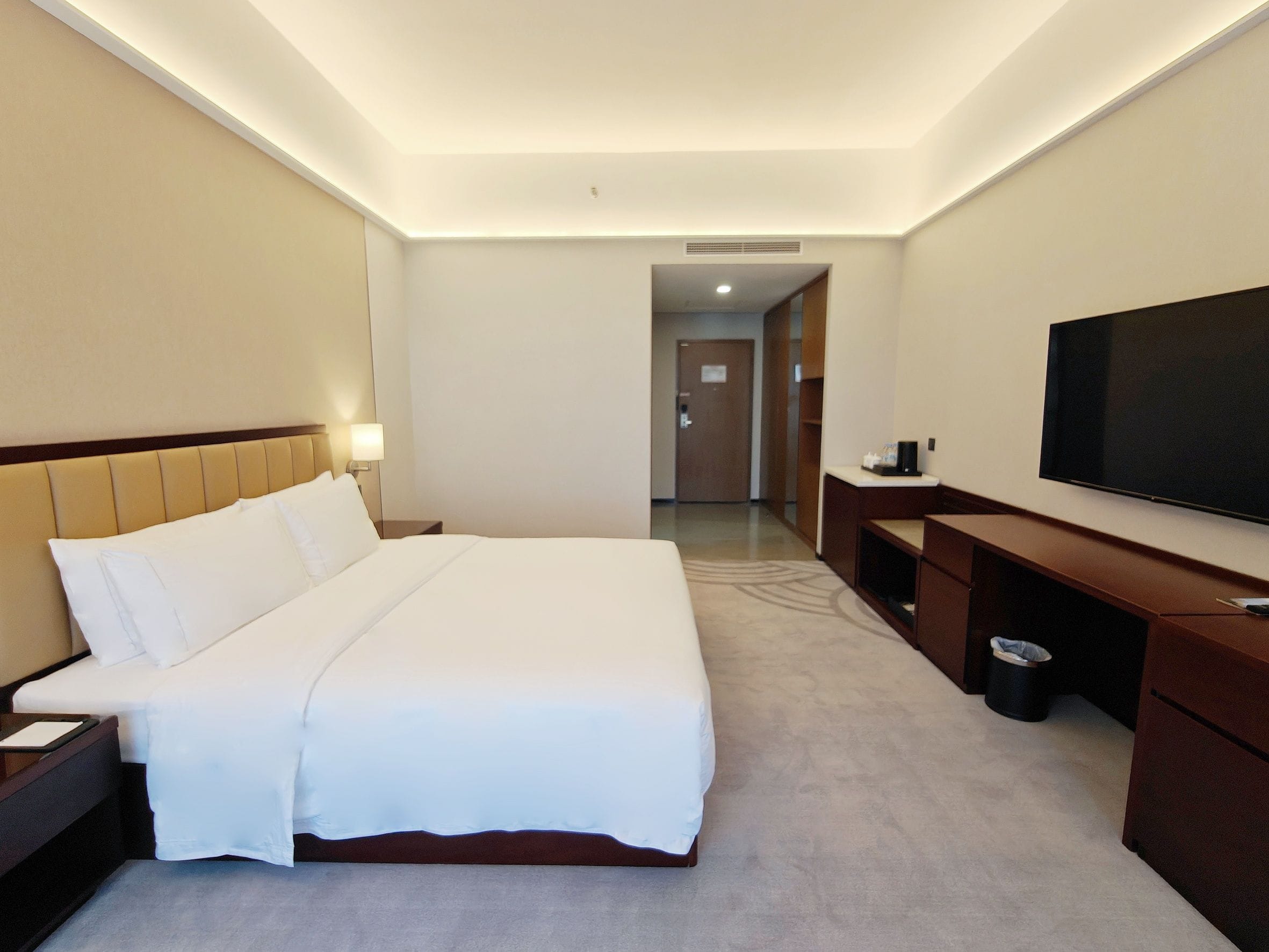 A hotel room with a large bed, a television, a desk, and a trash bin.