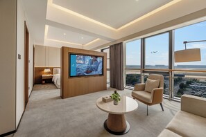 Habitació d'hotel moderna amb un televisor gran, un sofà confortable, una taula petita i vista a l'aeroport.