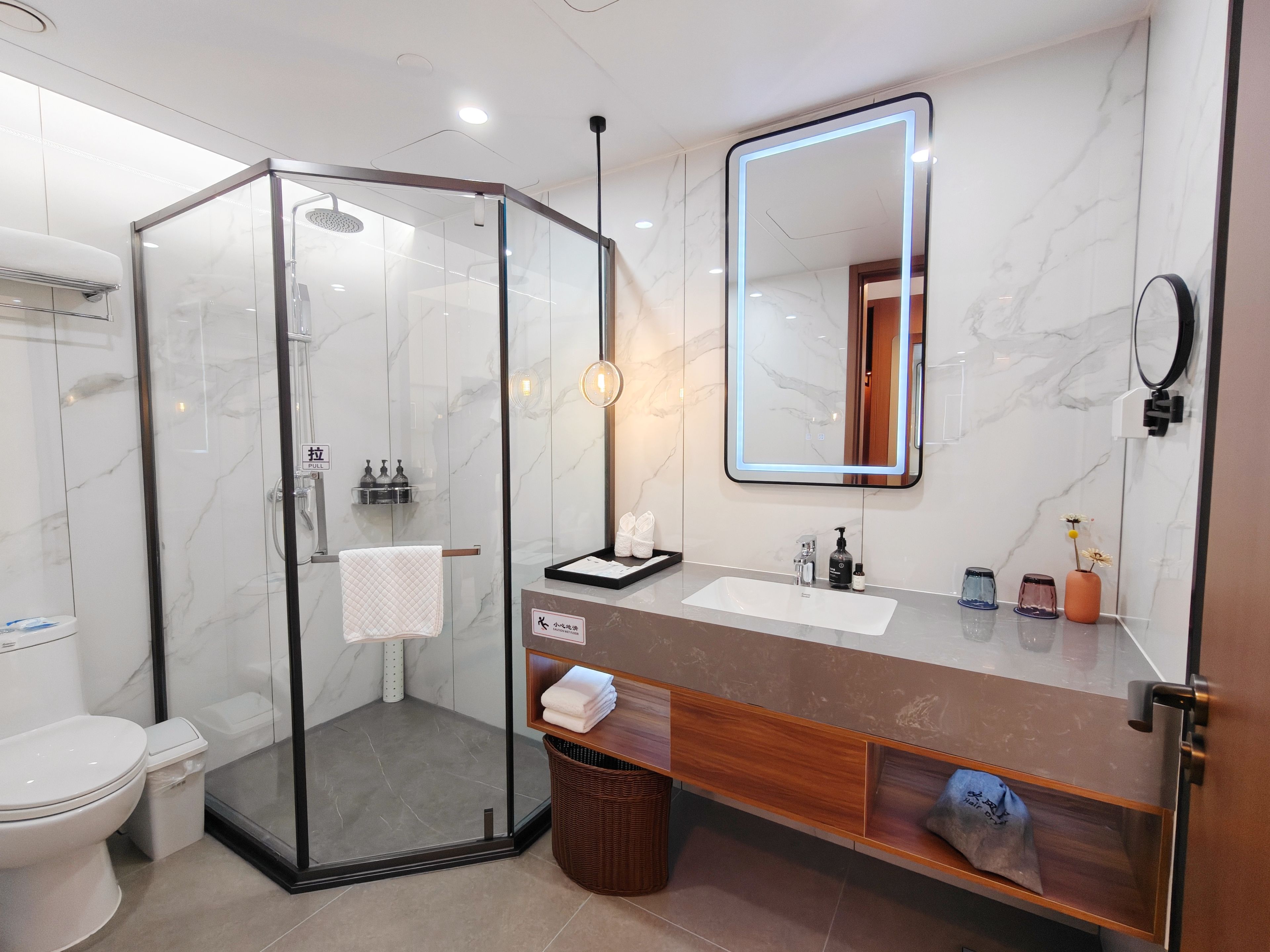 A modern bathroom with a glass-enclosed shower, a vanity with a marble countertop, and a large mirror with integrated lighting.