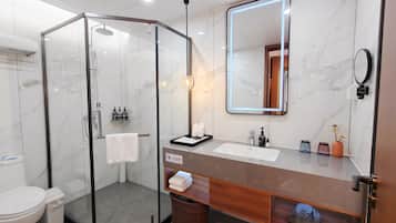 A modern bathroom with a glass-enclosed shower, a vanity with a marble countertop, and a large mirror with integrated lighting.