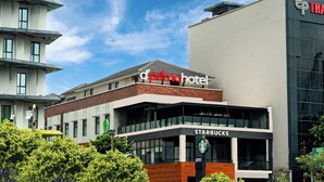 A modern hotel with a 'd'primohotel' sign, a Starbucks, and a 'TRAFF' sign on adjacent buildings. - d'primahotel Harmoni Jakarta-Hayam Wuruk (Jakarta)