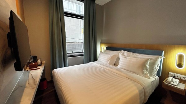 A hotel room with a bed, a bedside table with a lamp, a telephone, and a window with curtains.