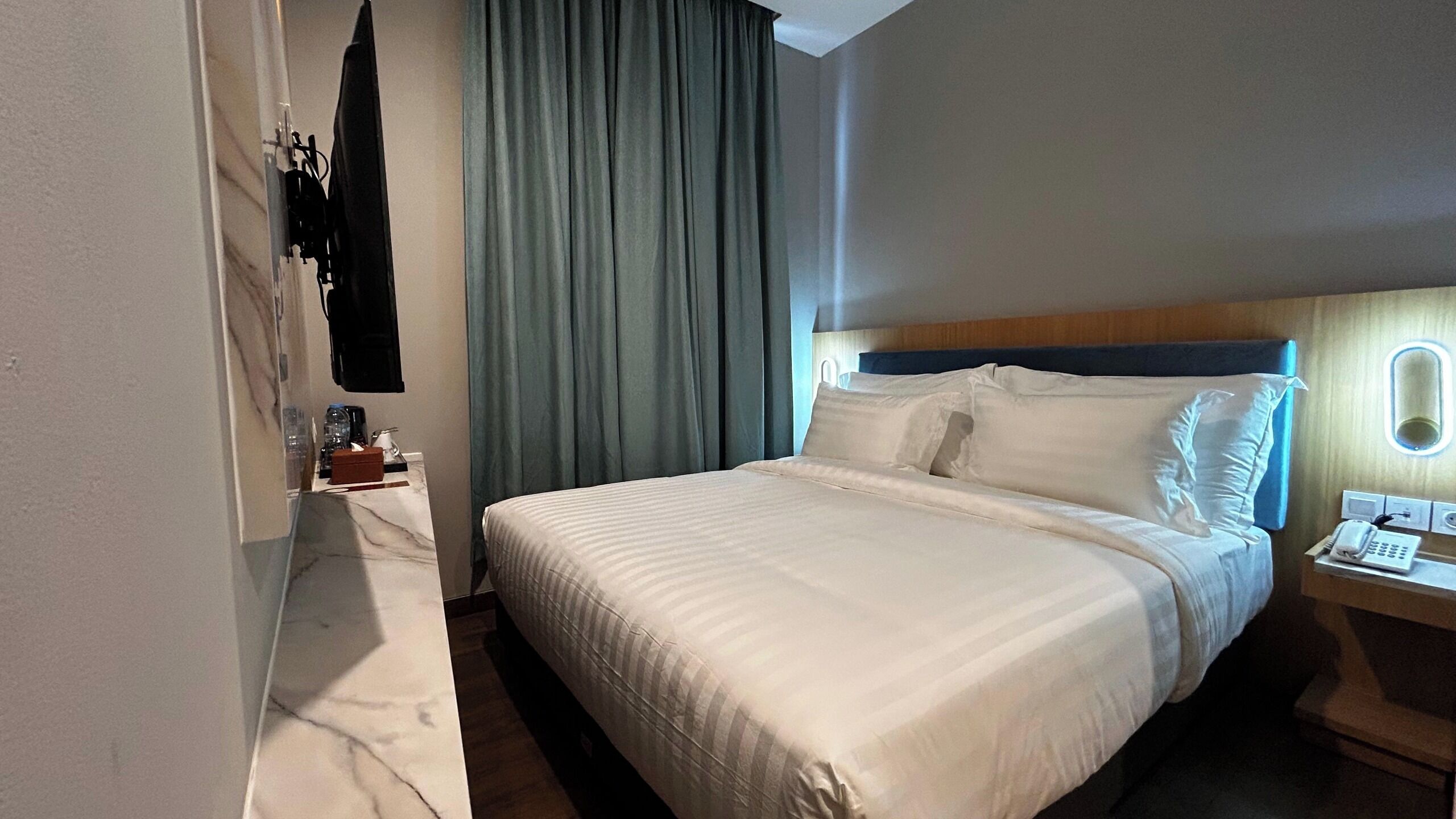 A hotel room with a bed, a bedside table with a lamp, a phone, and a mirror.