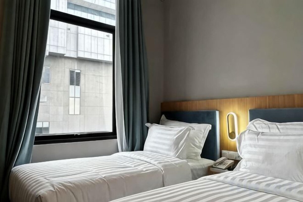 Une chambre d’hôtel avec deux lits, une table de chevet, une lampe et une fenêtre avec des rideaux.