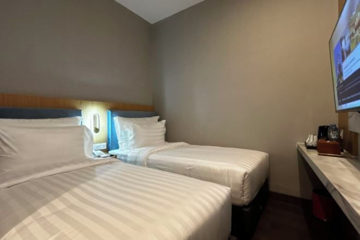 A hotel room with two beds, a TV on the wall, and a small desk with a lamp.