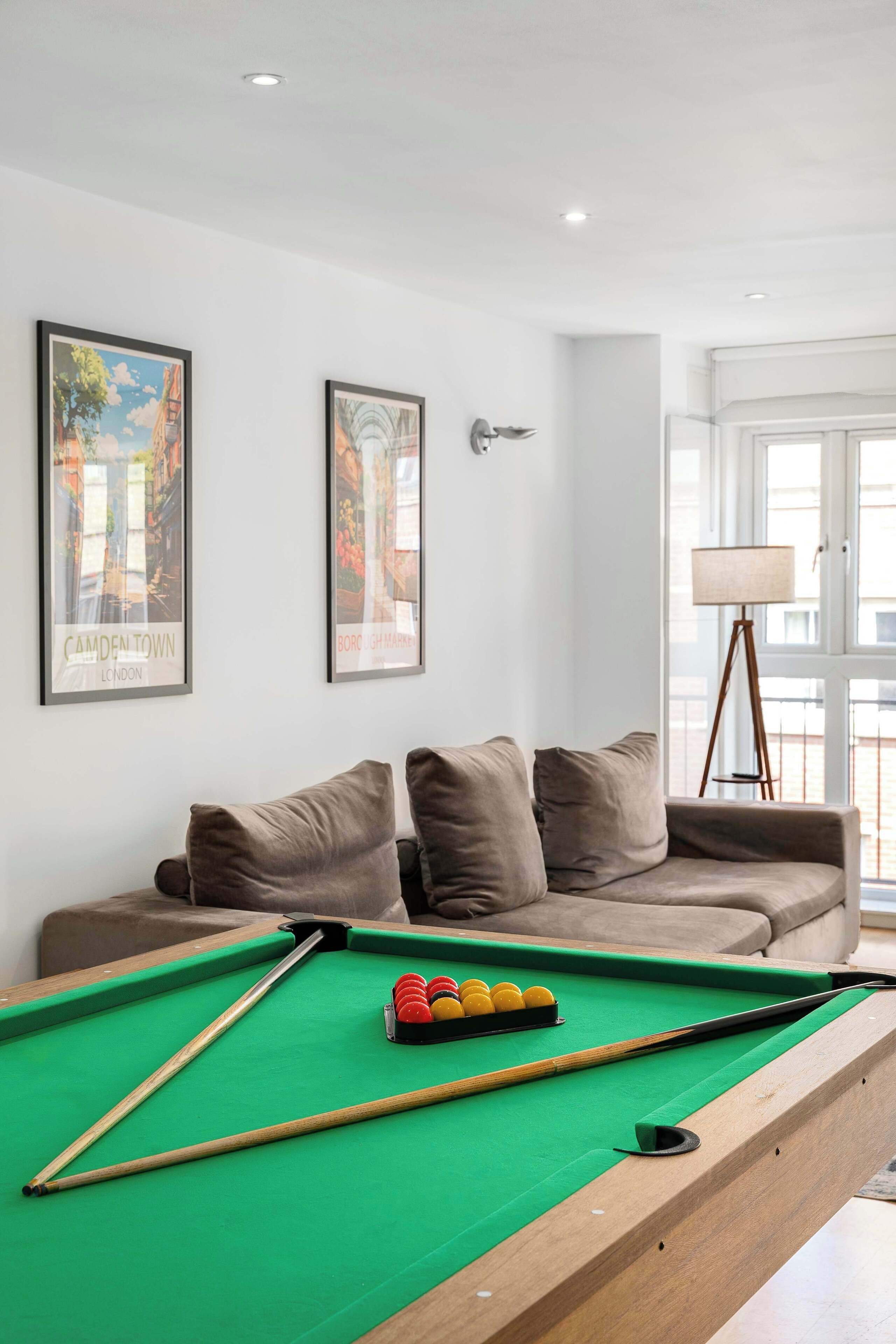 A pool table with balls, a sofa, and two framed pictures on the wall.