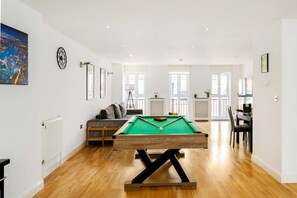 A spacious room with a pool table, a sofa, a dining table, and a large window.