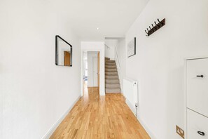 A hallway with wooden flooring, a white radiator, a coat rack, and a staircase leading to another room. - Spacious 3BR Shoreditch ApartM, 2Baths, 2 Balconies 150 SqM Sleeps Family of 6 (Greater London)