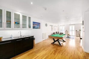 A modern kitchen with a pool table, wooden flooring, and a cityscape view.