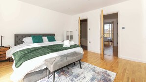 A bedroom with a bed, a bench, a bedside table, a lamp, and a door leading to a bathroom. - Spacious 3BR Shoreditch ApartM, 2Baths, 2 Balconies 150 SqM Sleeps Family of 6 (Greater London)