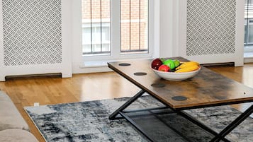 Ein modernes Wohnzimmer mit einem Esstisch, einem gemusterten Teppich und einer Schale Obst.