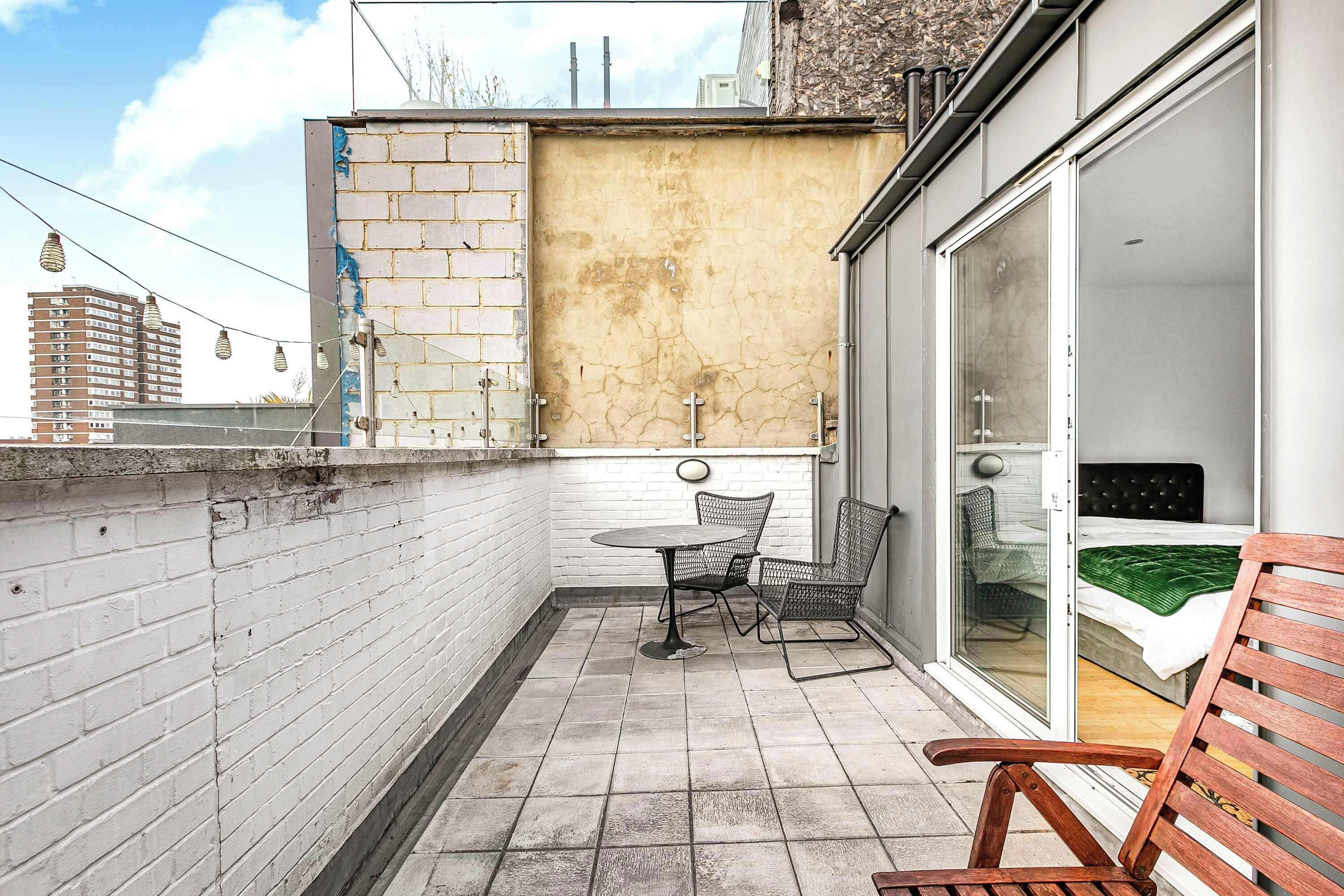 A balcony with a table and chairs, a wooden bench, and a sliding glass door leading to a bedroom.