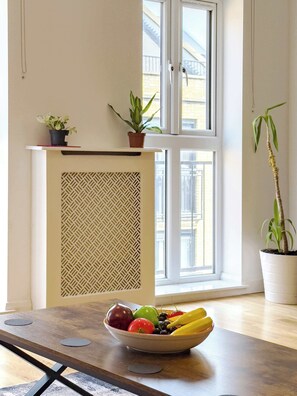 A room with a dining table, a bowl of fruit, a potted plant, and a window with a view of buildings. - Spacious 3BR Shoreditch ApartM, 2Baths, 2 Balconies 150 SqM Sleeps Family of 6 (Greater London)