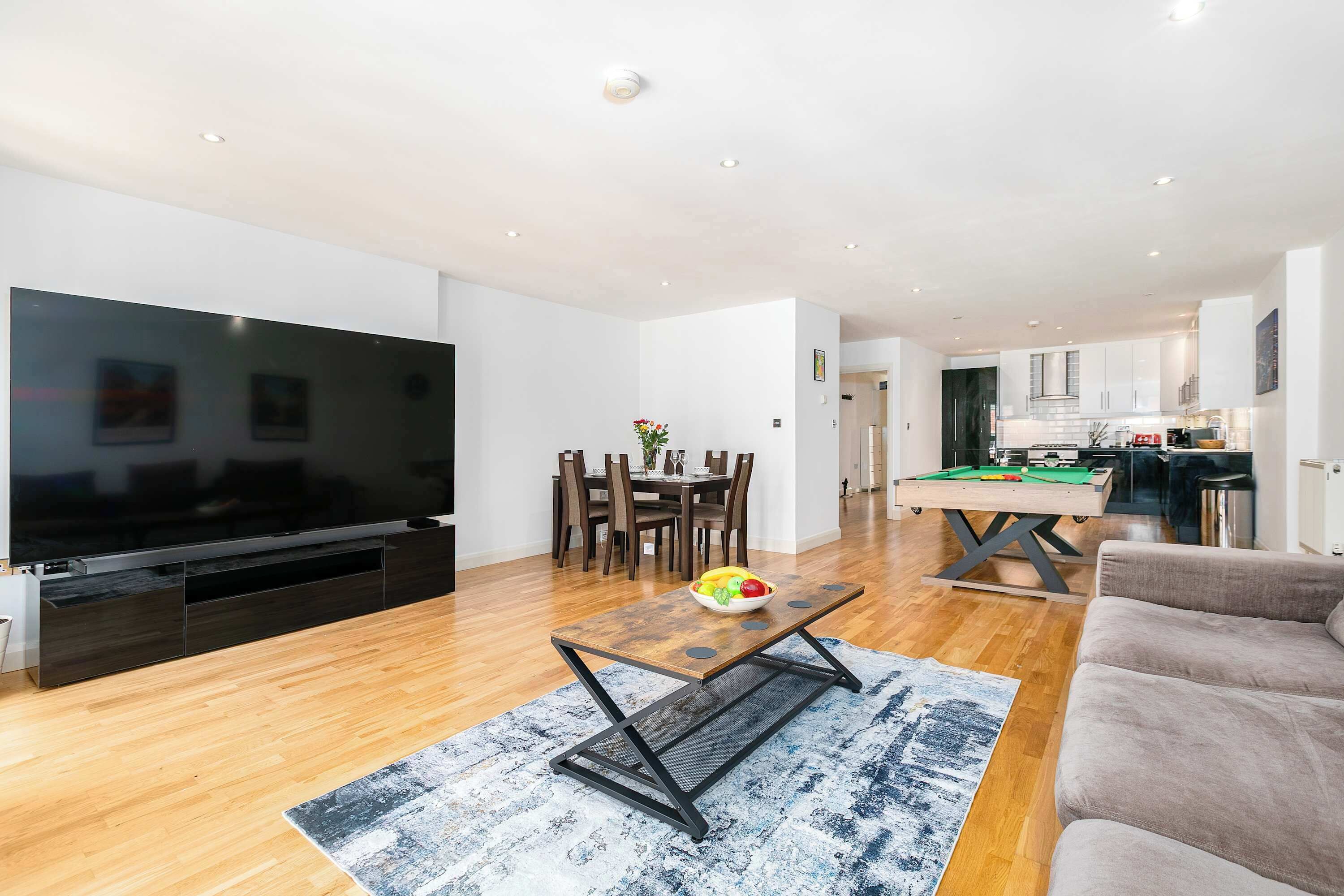 Ein modernes Wohnzimmer mit Flachbildfernseher, einem Esstisch mit Stühlen, einem Billardtisch und einer Couch.