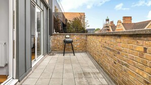 A narrow outdoor space with a brick wall, a small table, and a chair. - Spacious 3BR Shoreditch ApartM, 2Baths, 2 Balconies 150 SqM Sleeps Family of 6 (Greater London)