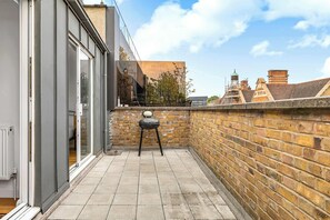 A narrow outdoor space with a brick wall, a small table, and a chair. - Spacious 3BR Shoreditch ApartM, 2Baths, 2 Balconies 150 SqM Sleeps Family of 6 (Greater London)