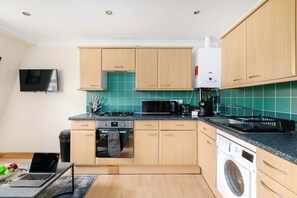 A modern kitchen with wooden cabinets, a microwave, a stove, and a washing machine.