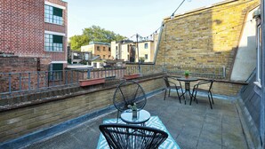 Une terrasse sur le toit, avec une table et des chaises, un ventilateur et une vue sur les bâtiments voisins.