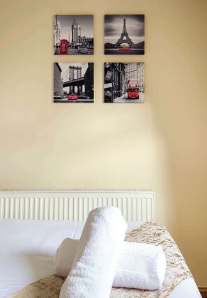 A hotel room with a bed, two wall-mounted pictures of famous landmarks, and a white radiator. - Cute Old Street Studio Suit Couple (Greater London)