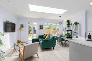Un salon moderne avec un canapé vert, une table basse en verre et un coin repas comprenant une table et des chaises blanches.
