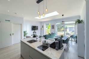 A modern kitchen with a central island, a dining area with a sofa, and a view of the outdoors.