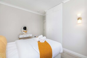 Ein Hotelzimmer mit Bett, Nachttisch mit Spiegel, Wandleuchte und Tür.