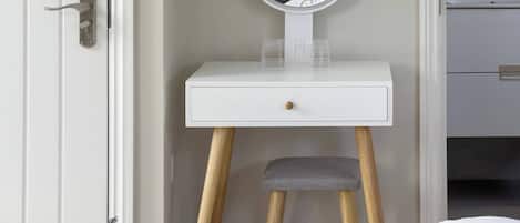 A room with a white door, a bedside table with a mirror, a small drawer, and a bed with a white and black patterned blanket.