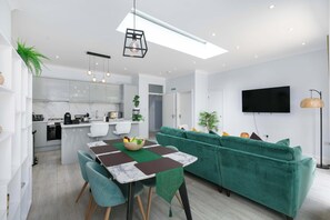 A modern living space with a dining area, kitchen, and a green sofa.
