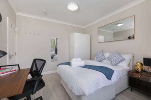 A hotel room with a bed, bedside table, chair, desk, and a mirror.